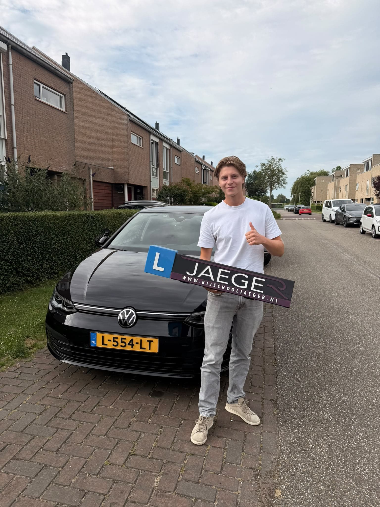 Geslaagde leerling met een Jaeger-bord voor de lesauto